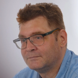 Martin von Pobrucki sitzt vor einem grauen Hintergrund und lächelt.