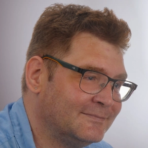 Martin von Pobrucki sitzt vor einem grauen Hintergrund und lächelt.